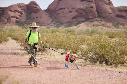 Rob and his guide dog, Kent, jogging on a red sandy trail in Papago Park, Phoenix, with desert brush and large hills in the background.